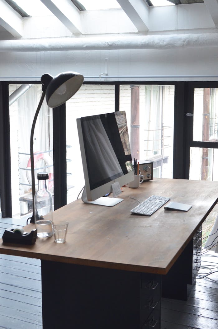 Modern computer placed on desk with lamp and radio in office